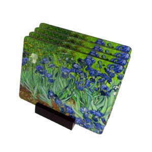 May include: Set of four glass coasters featuring a vibrant painting of blue irises against a green background. The coasters are stacked and displayed on a black stand.