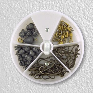 May include: A white round plastic container with six compartments filled with fishing tackle. The compartments contain sinkers, hooks, and swivels.
