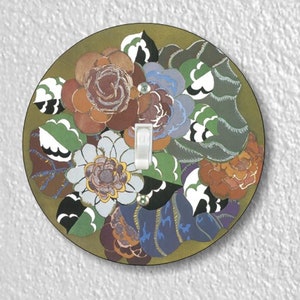 May include: A round light switch cover with a floral design. The cover features a variety of flowers in shades of red, orange, yellow, blue, and green. The flowers are arranged in a circular pattern around a white light switch.