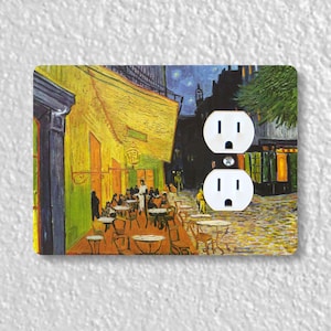 May include: A decorative double electrical outlet cover featuring a print of Van Gogh's "Cafe Terrace at Night." The artwork depicts a yellow cafe with patrons, tables, and chairs on a cobblestone street under a starry night sky. The outlet cover is white.