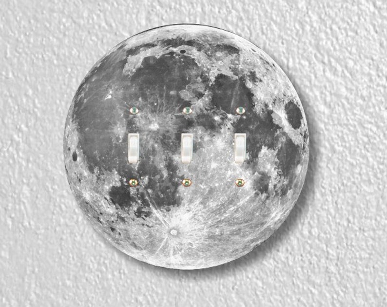 May include: A light switch cover featuring a black and white image of the moon with three white toggle switches and three small green eyes.