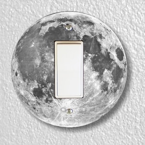 May include: A round light switch cover with a black and white image of the moon.