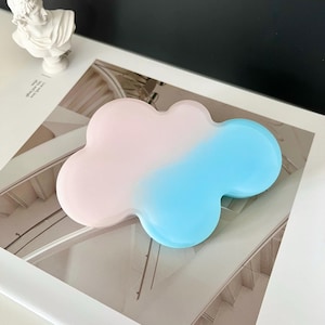 May include: A cloud-shaped, ombre-coloured silicone phone stand. The stand is pink on top and fades to blue on the bottom.