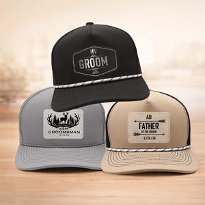 May include: Three baseball caps with personalized patches. One black cap features "GROOM" text, a gray cap says "GROOMSMAN", and a tan cap reads "FATHER OF THE GROOM". Each cap has a rope detail and a flat brim.