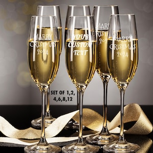 May include: Set of six champagne flutes with personalized engravings. The flutes are filled with a golden liquid and are arranged on a gold ribbon. The engravings include "Marry Christmas 2024", "Your Custom Text", and "Marry Christmas 2024".