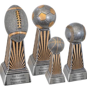 May include: Four sports-themed trophies with silver and gold accents. The trophies feature a football, soccer ball, basketball, and baseball atop decorative bases with text that reads "Your Custom Personalization Engraved Here."
