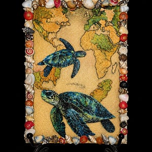 May include: A rectangular artwork featuring a world map with two sea turtles. The map is gold and green, with the turtles in shades of blue and green. The artwork is framed with various seashells.