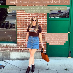 Op de afbeelding: Een bruin T-shirt met Monument Valley-opdruk, een blauwe spijkerrok met knoopsluiting en zakken, bruine enkellaarsjes en een bruine tas van veganistisch leer. Tekstoverlays bevatten Sample Mini Custom Curated Style Box, Inspiration: western boho style, elevated every day pieces, National Park tee shirts, en Pieces: Monument Valley graphic tee, Free People denim skirt, brown ankle boots, vegan leather reversabile tote.