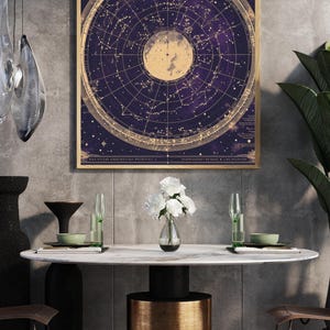 May include: A framed celestial map print with a gold frame. The map features a circular design with constellations and celestial bodies in gold against a deep purple background. The print is displayed above a modern dining table.