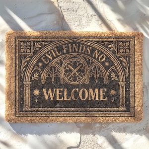 Op de afbeelding: Een rechthoekige kokosmat met een donkerbruin ontwerp en de tekst "EVIL FINDS NO WELCOME" in een gotisch lettertype. Het ontwerp bevat decoratieve bogen, sterren en een gekruist zwaardembleem. De mat heeft een lichtbruine rand.
