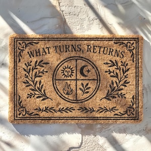 May include: Rectangular coir doormat with the text "WHAT TURNS, RETURNS" in black. The centre features a circular design with sun, moon, fire, and plant symbols. Decorative black leaf patterns frame the text and design.