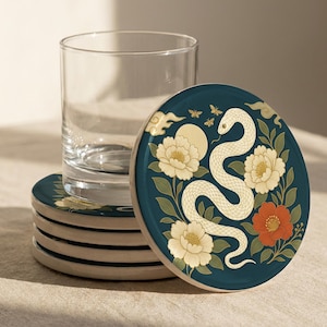 May include: Set of four round ceramic coasters with a dark teal background. Each coaster features a white snake design with cream-colored flowers and a red flower. A clear glass sits next to the coasters.