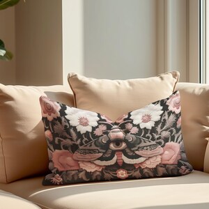 Gothic moth eye botanical lumbar pillow with mystical embroidered wings on dark fabric. Cottagecore throw pillow featuring protective moth symbol surrounded by pink roses, white wildflowers & sacred botanicals. Witchy home decor with medieval tapestry aesthetic. Perfect for dark academia spaces, bohemian decor & occult art lovers. 20x12 lumbar size.