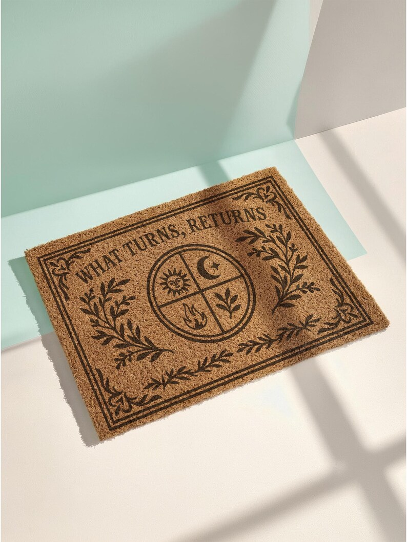 Natural coir doormat featuring "What Turns, Returns" text with sacred elemental symbolism including sun, crescent moon, flames, and botanical sprigs arranged in protective circular mandala design. Four classical elements represented in quadrants surrounded by intricate corner flourishes and leafy botanical borders. Perfect witchy welcome mat for pagan home decor, spiritual protection, and mystical entryway styling.