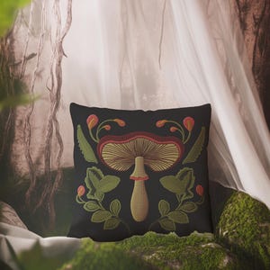 A dark woven pillow with a detailed embroidered mushroom and botanical design in deep red, green, and gold tones. Made with a cotton-poly blend.