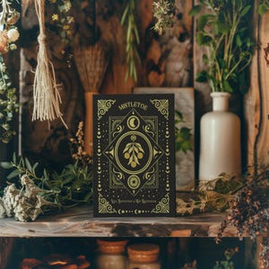 Luxurious black Yule card featuring golden mistletoe design, moon phases, and stars. "Mistletoe" and "For Protection & New Beginnings" in ornate gold text.