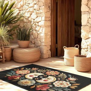 Witchy outdoor doormat featuring a central all-seeing eye, crescent moons, and floral details in an embroidery-style design. This weatherproof welcome mat measures 26x18 inches and is ideal for porches or patio entries. Symbolic celestial motifs offer intuitive protection and spiritual elegance for magical home decor.