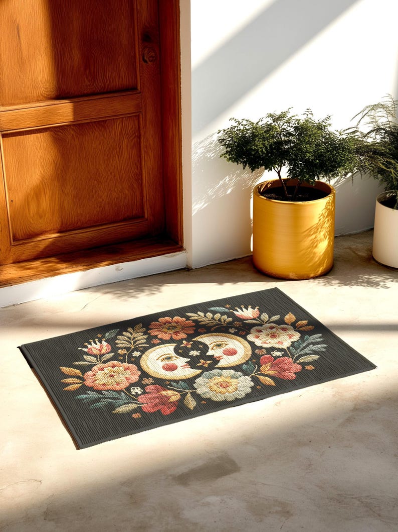 Witchy outdoor doormat featuring a central all-seeing eye, crescent moons, and floral details in an embroidery-style design. This weatherproof welcome mat measures 26x18 inches and is ideal for porches or patio entries. Symbolic celestial motifs offer intuitive protection and spiritual elegance for magical home decor.