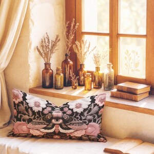 Gothic moth eye botanical lumbar pillow with mystical embroidered wings on dark fabric. Cottagecore throw pillow featuring protective moth symbol surrounded by pink roses, white wildflowers & sacred botanicals. Witchy home decor with medieval tapestry aesthetic. Perfect for dark academia spaces, bohemian decor & occult art lovers. 20x12 lumbar size.