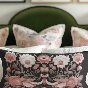 Gothic moth eye botanical lumbar pillow with mystical embroidered wings on dark fabric. Cottagecore throw pillow featuring protective moth symbol surrounded by pink roses, white wildflowers & sacred botanicals. Witchy home decor with medieval tapestry aesthetic. Perfect for dark academia spaces, bohemian decor & occult art lovers. 20x12 lumbar size.