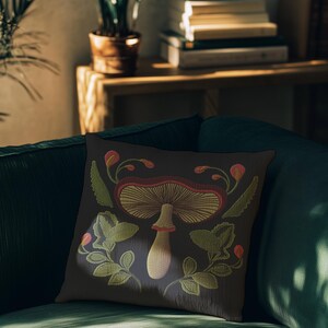 A dark woven pillow with a detailed embroidered mushroom and botanical design in deep red, green, and gold tones. Made with a cotton-poly blend.