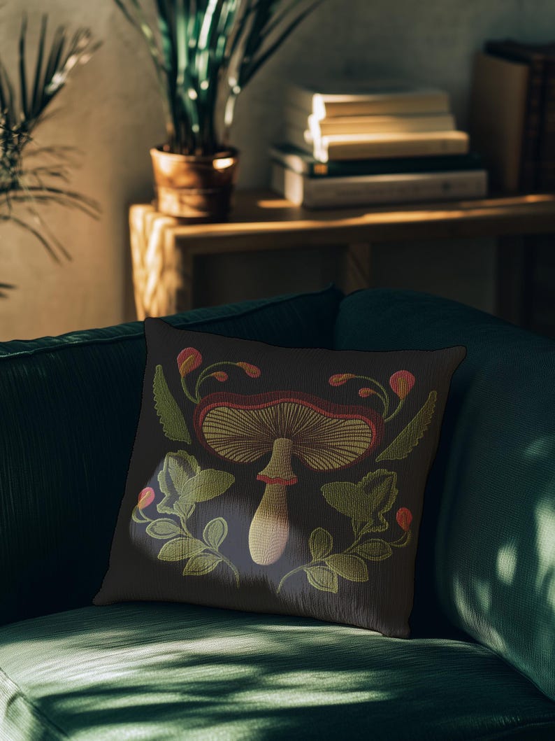 A dark woven pillow with a detailed embroidered mushroom and botanical design in deep red, green, and gold tones. Made with a cotton-poly blend.