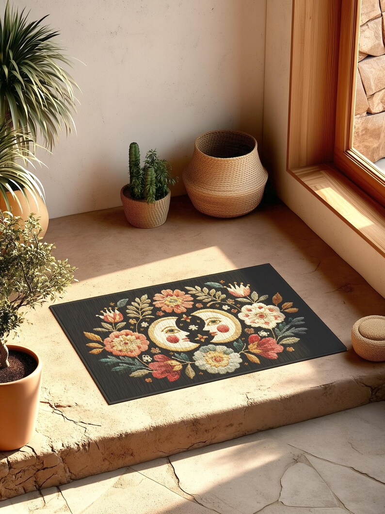 Witchy outdoor doormat featuring a central all-seeing eye, crescent moons, and floral details in an embroidery-style design. This weatherproof welcome mat measures 26x18 inches and is ideal for porches or patio entries. Symbolic celestial motifs offer intuitive protection and spiritual elegance for magical home decor.
