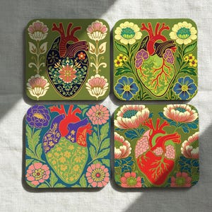 May include: Set of four square coasters featuring stylized anatomical heart designs. Each coaster has a different heart design with floral and botanical elements in shades of red, green, blue, and pink, set against a green background.