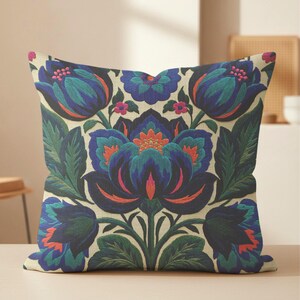 May include: A square throw pillow featuring a cream-colored background with a symmetrical floral pattern. The design includes large, stylized blue and teal flowers with dark green leaves and vibrant orange and pink accents throughout the print.