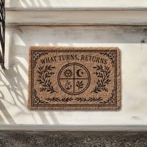 Natural coir doormat featuring "What Turns, Returns" text with sacred elemental symbolism including sun, crescent moon, flames, and botanical sprigs arranged in protective circular mandala design. Four classical elements represented in quadrants surrounded by intricate corner flourishes and leafy botanical borders. Perfect witchy welcome mat for pagan home decor, spiritual protection, and mystical entryway styling.