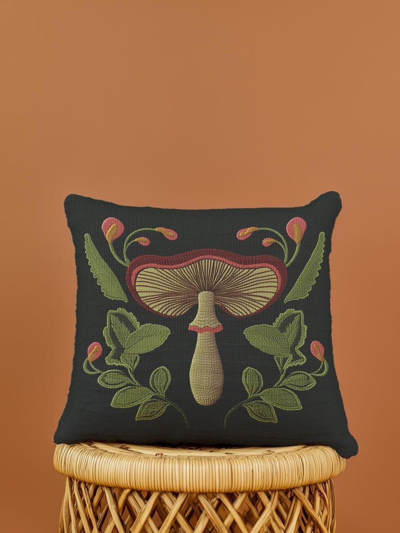 A dark woven pillow with a detailed embroidered mushroom and botanical design in deep red, green, and gold tones. Made with a cotton-poly blend.