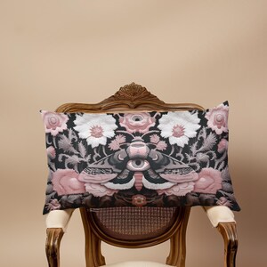 Gothic moth eye botanical lumbar pillow with mystical embroidered wings on dark fabric. Cottagecore throw pillow featuring protective moth symbol surrounded by pink roses, white wildflowers & sacred botanicals. Witchy home decor with medieval tapestry aesthetic. Perfect for dark academia spaces, bohemian decor & occult art lovers. 20x12 lumbar size.