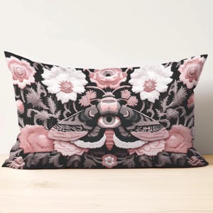 Gothic moth eye botanical lumbar pillow with mystical embroidered wings on dark fabric. Cottagecore throw pillow featuring protective moth symbol surrounded by pink roses, white wildflowers & sacred botanicals. Witchy home decor with medieval tapestry aesthetic. Perfect for dark academia spaces, bohemian decor & occult art lovers. 20x12 lumbar size.