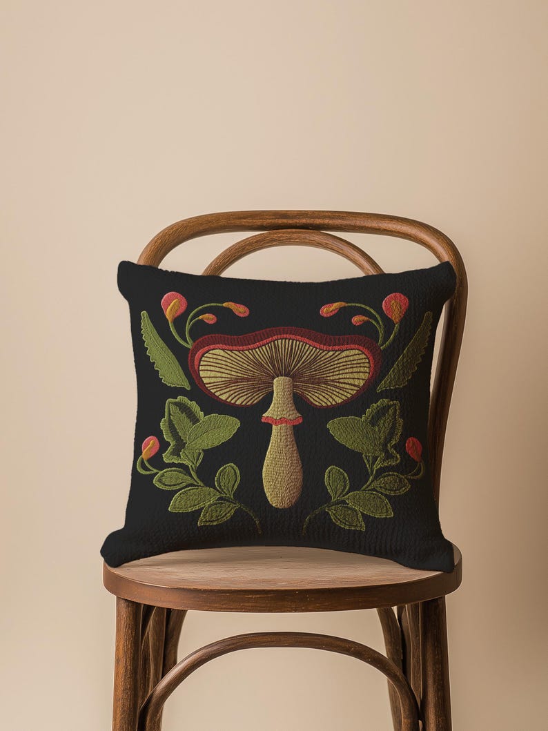 A dark woven pillow with a detailed embroidered mushroom and botanical design in deep red, green, and gold tones. Made with a cotton-poly blend.