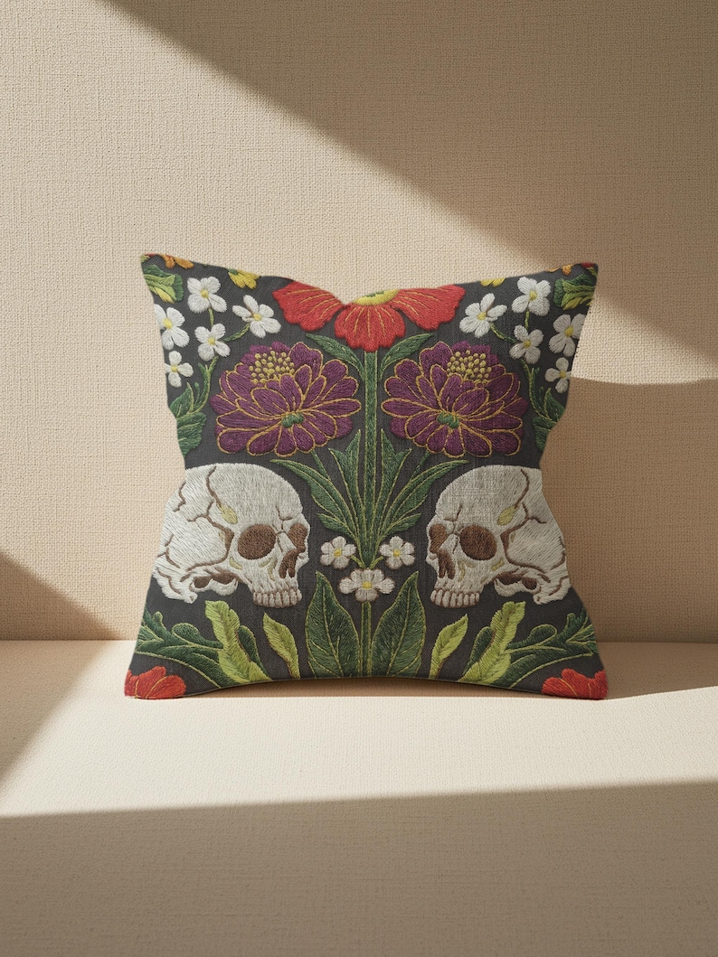 Grimoire and Goblet gothic pillow cover featuring mirrored ivory human skulls surrounded by detailed floral and botanical elements including deep red flowers, purple blooms with gold outlining, small white blossoms, and layered green foliage, arranged in a symmetrical composition on a charcoal background, designed with a high-detail faux embroidery print that mimics stitched texture while remaining smooth, creating a dark academia and gothic botanical aesthetic decorative cushion cover