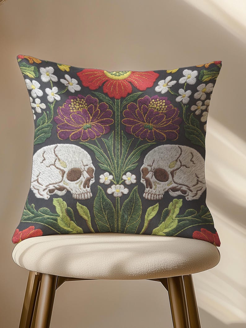 Grimoire and Goblet gothic pillow cover featuring mirrored ivory human skulls surrounded by detailed floral and botanical elements including deep red flowers, purple blooms with gold outlining, small white blossoms, and layered green foliage, arranged in a symmetrical composition on a charcoal background, designed with a high-detail faux embroidery print that mimics stitched texture while remaining smooth, creating a dark academia and gothic botanical aesthetic decorative cushion cover