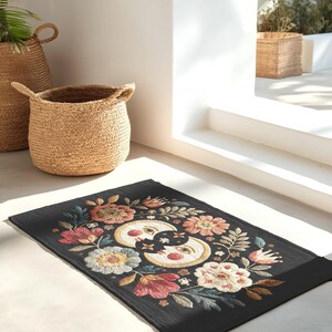 Witchy outdoor doormat featuring a central all-seeing eye, crescent moons, and floral details in an embroidery-style design. This weatherproof welcome mat measures 26x18 inches and is ideal for porches or patio entries. Symbolic celestial motifs offer intuitive protection and spiritual elegance for magical home decor.