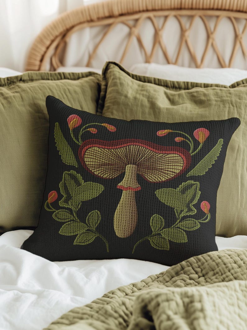 A dark woven pillow with a detailed embroidered mushroom and botanical design in deep red, green, and gold tones. Made with a cotton-poly blend.