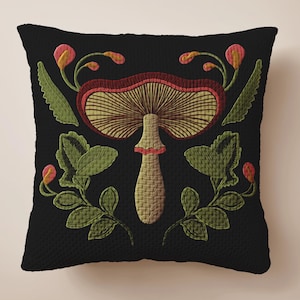 A dark woven pillow with a detailed embroidered mushroom and botanical design in deep red, green, and gold tones. Made with a cotton-poly blend.