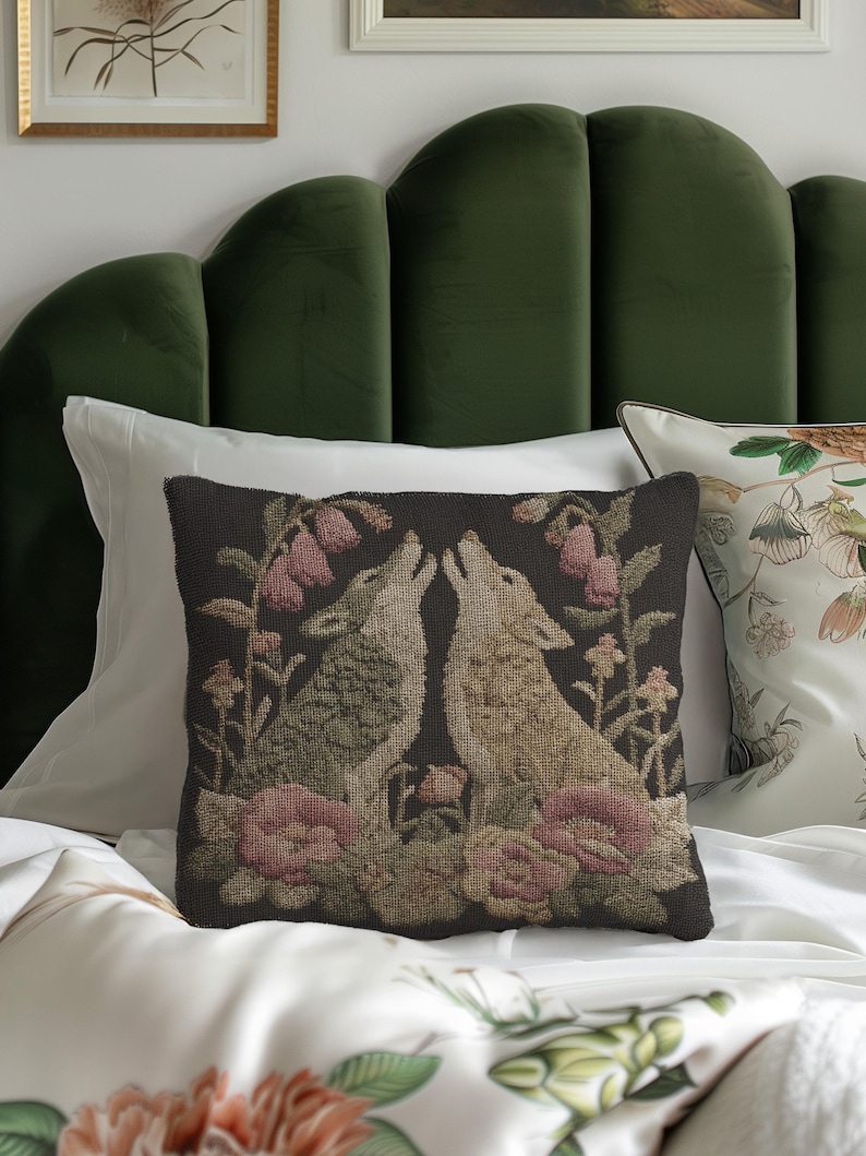 A square woven tapestry pillow with two howling wolves on a black background. The wolves are surrounded by pink and green botanical flowers, creating a vintage, folkloric scene. This decorative cushion is perfect for cottagecore, dark academia, and gothic home decor.