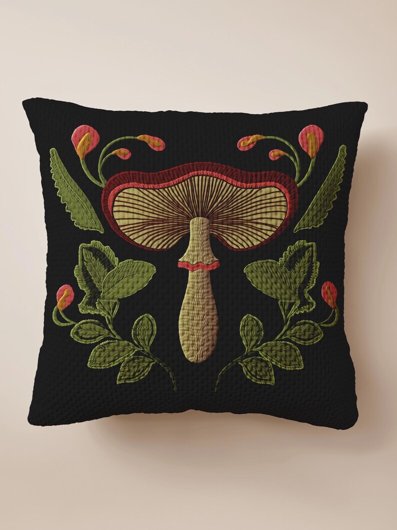 A dark woven pillow with a detailed embroidered mushroom and botanical design in deep red, green, and gold tones. Made with a cotton-poly blend.