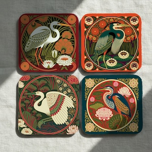 May include: A set of four square coasters featuring detailed illustrations of herons and egrets surrounded by lotus flowers and aquatic plants. Each coaster displays a unique color palette including deep red, orange, green, and dark teal backgrounds.
