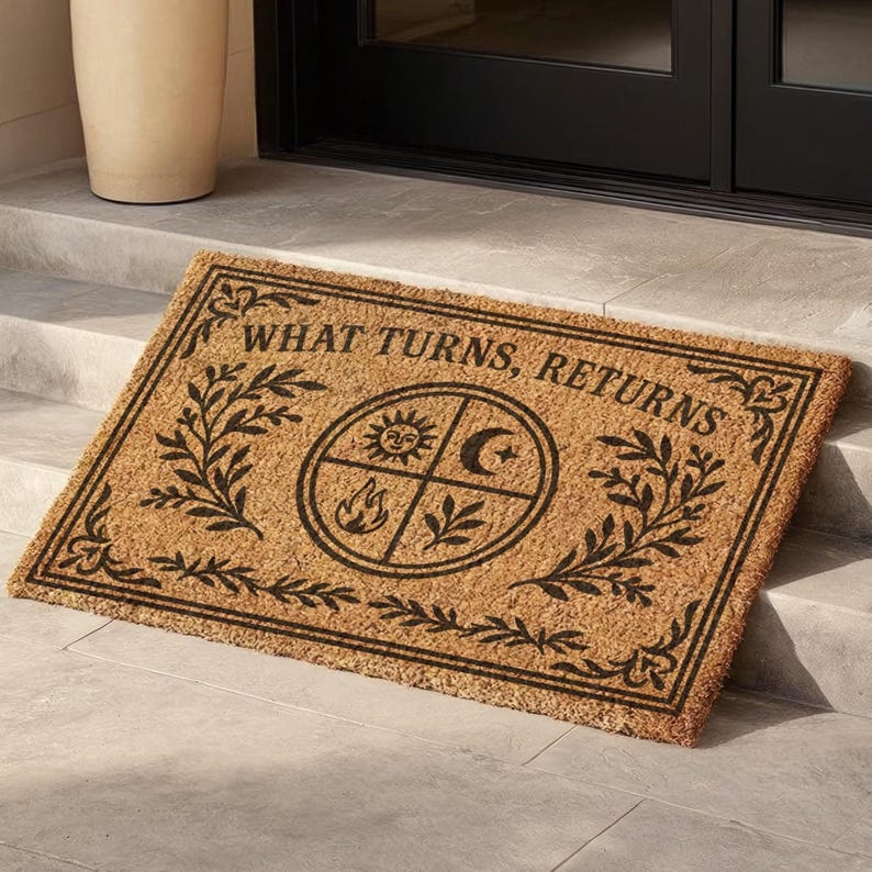 Natural coir doormat featuring "What Turns, Returns" text with sacred elemental symbolism including sun, crescent moon, flames, and botanical sprigs arranged in protective circular mandala design. Four classical elements represented in quadrants surrounded by intricate corner flourishes and leafy botanical borders. Perfect witchy welcome mat for pagan home decor, spiritual protection, and mystical entryway styling.