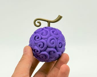 May include: A purple, spherical fruit with a swirling pattern and a gold-colored stem. The fruit is held in a hand against a white background. The design is reminiscent of a fictional item.