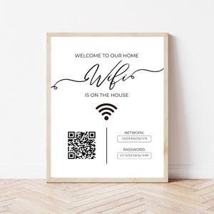 以下が含まれることがあります： 「WELCOME TO OUR HOME Wifi IS ON THE HOUSE」と黒い文字で書かれた、額縁に入った白いサイン。QRコード、Wi-Fiのシンボル、ネットワークとパスワードの詳細が含まれています。フレームは明るい木の色です。