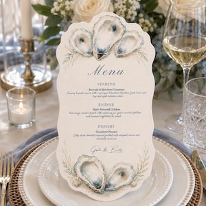 May include: A scalloped-edge menu card featuring watercolor illustrations of oysters at the top and bottom. The text reads Menu, Starter Burrata & Heirloom Tomatoes, Entree Herb-Roasted Chicken, Dessert Chocolate Mousse, and the names Gisella & Bradly.