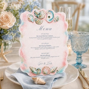 May include: A scalloped-edge menu card featuring watercolor illustrations of seashells in shades of pink, blue, and tan. The text reads Menu, Starter Burrata & Heirloom Tomatoes, Entree Herb-Roasted Chicken, Dessert Chocolate Mousse, and Gaelle & Bradly.