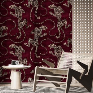 May include: Wallpaper featuring a repeating pattern of tan and black spotted leopards on a deep burgundy background. The leopards are depicted in various leaping poses with long, curved tails, creating a continuous, dense graphic design.