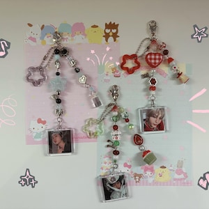 May include: Two beaded keychains with photo inserts. One keychain has a star and a clear bottle charm, the other has a red heart and a cupcake charm. Both have silver chains and various beads.