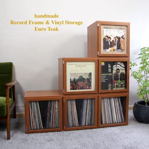 Pode incluir: Unidade de armazenamento de vinil e moldura Euro Teak feita à mão. A unidade é feita de madeira e tem um acabamento castanho quente. A unidade foi projetada para guardar discos de vinil e possui portas de vidro. A unidade está disposta em uma configuração escalonada.